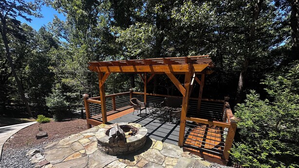 Eine hölzerne Pergola mit einem Steinkamin in bewaldeter Landschaft.