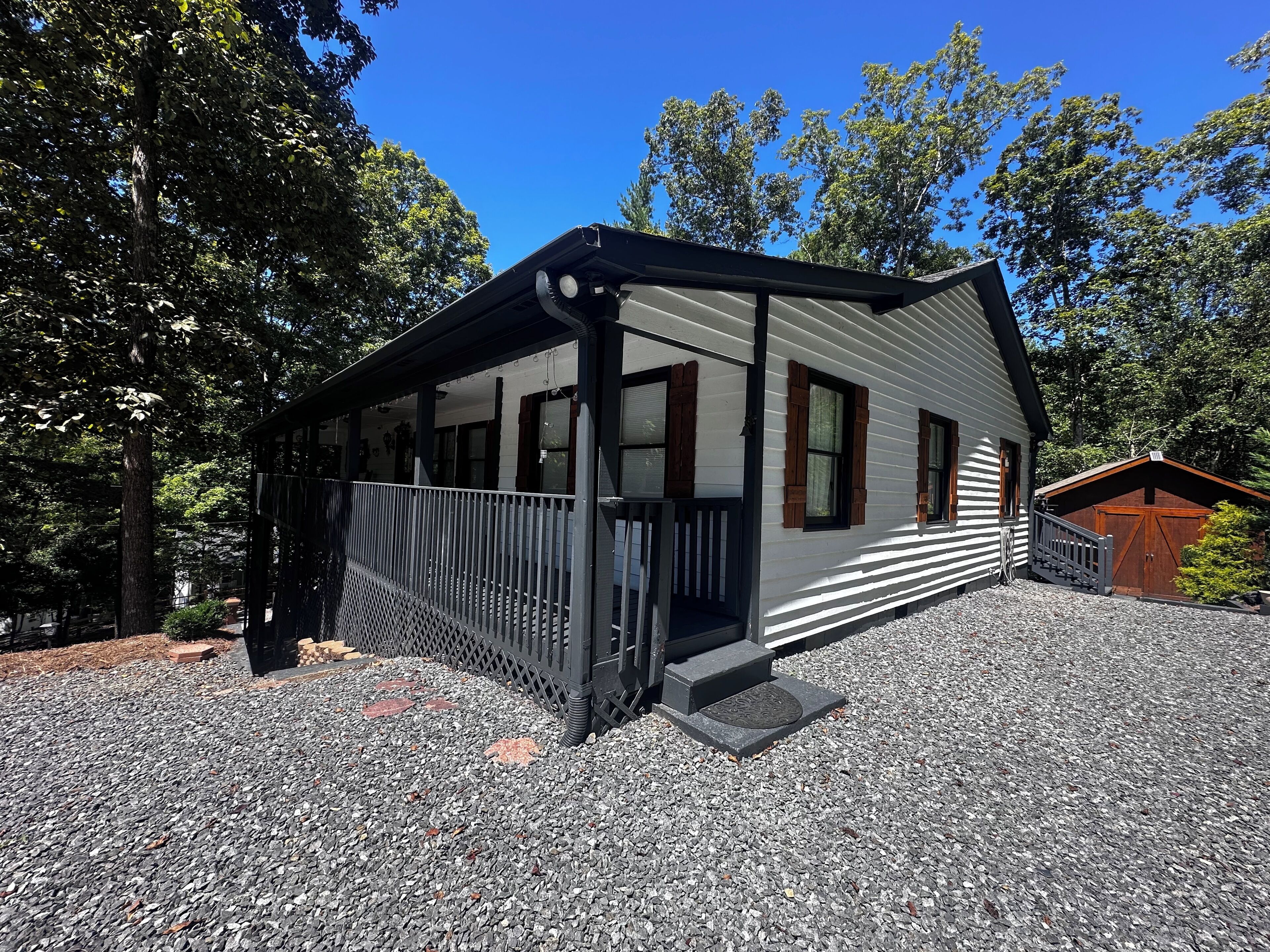 A cabin with a covered porch, a small attached garage, and a gravel driveway.