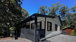 Eine Hütte mit überdachter Veranda, einer kleinen angeschlossenen Garage und einem Schotterweg.