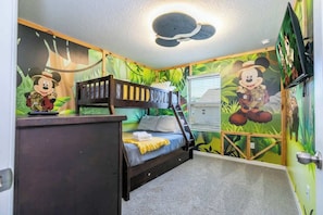 Un dormitorio infantil con una cama nido, un escritorio y murales con temática de Mickey Mouse.
