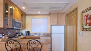 Una cocina compacta con armarios de madera, microondas, refrigerador, pileta y dos sillas.