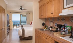 A hotel room with a balcony, a bed, a kitchenette, and a view of the ocean.