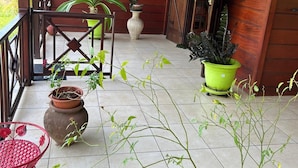 Un balcón de madera con plantas en macetas, una silla roja y un suelo de baldosas.