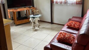 Una sala de estar con televisor, sofá, una mesita decorativa y una ventana con cortinas.