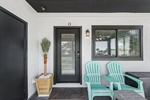 A black door with the number 13, a potted plant, two green chairs, and a window with blinds.