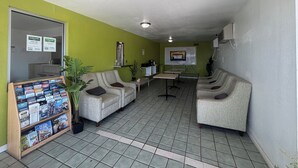 A reception area with a green wall, a reception desk, a seating area with two sofas, a small table, and a display of travel brochures. - Parkside Inn by PHG - Sweetwater (Sweetwater)