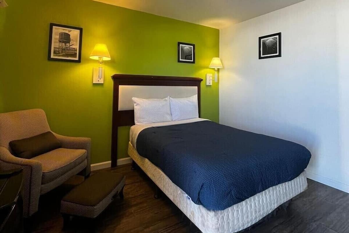 A hotel room with a bed, a chair, and two wall-mounted lamps.