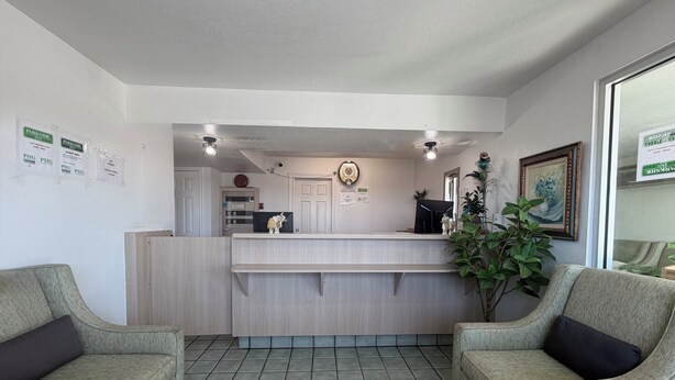 A reception area with a reception desk, two armchairs, a clock, and a framed picture on the wall. - Parkside Inn by PHG - Sweetwater (Sweetwater)