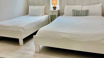 Een slaapkamer met twee eenpersoonsbedden en een tweepersoonsbed, een nachtkastje met lamp, een raam met zonwering, en een kamerbreed tapijt met een patroon.