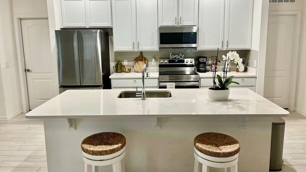 A modern kitchen with white cabinets, stainless steel appliances, and a central island with stools. - SPRING HAVEN RETREAT! A BEUTIFULL ANDSPOTLESS!! (Newberry)