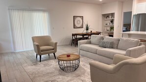 A modern living room with a beige armchair, a beige sofa, and a coffee table with a geometric base. - SPRING HAVEN RETREAT! A BEUTIFULL ANDSPOTLESS!! (Newberry)