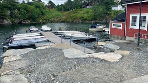 Laituri, jossa on useita veneitä, punainen rakennus valkoisilla koristeilla ja taustalla metsäinen rinnemaisema.