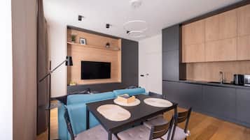 A modern living space with a dining area, a blue sofa, a flat-screen TV, and a kitchen area.