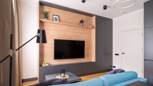A modern bedroom with a large TV mounted on a wooden wall, a blue sofa, a small side table, and a floor lamp.