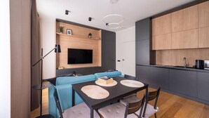 A modern living space with a dining area, a blue sofa, a flat-screen TV, and a kitchen area.