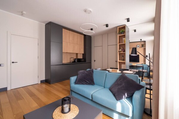 Un salon moderne avec un canapé bleu, une table basse et un coin cuisine équipé de placards et d’une table à manger.