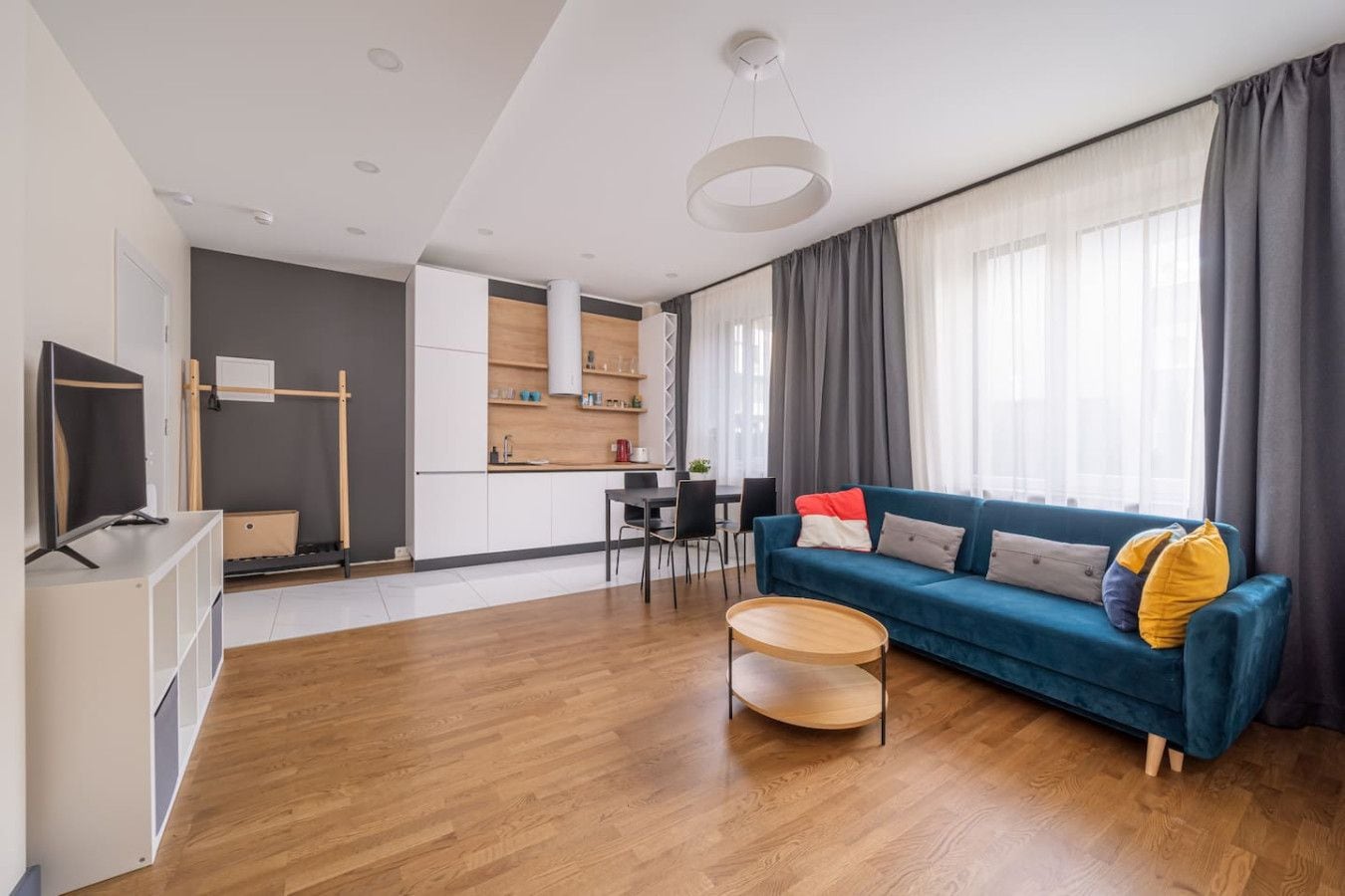 Una sala de estar moderna con un sofá azul, suelo de madera y un comedor con mesa y sillas.
