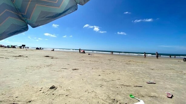Una playa con cielo despejado, un paraguas de estampado en zigzag y huellas en la arena.