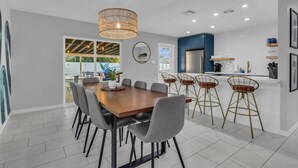 A modern kitchen with a dining area, featuring a wooden table, grey chairs, and a hanging light fixture.