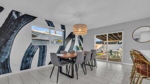 A modern dining area with a large abstract mural, a wooden dining table with chairs, and a view of the outdoors.