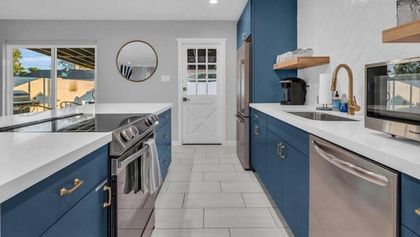 A modern kitchen with blue cabinets, stainless steel appliances, and a white countertop.