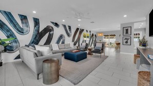 A modern living room with a grey sofa, blue ottoman, and abstract wall art.
