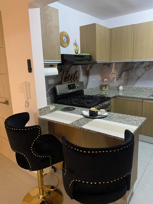 A modern kitchen with a marble backsplash, a built-in stove, and two black bar stools with gold studs.