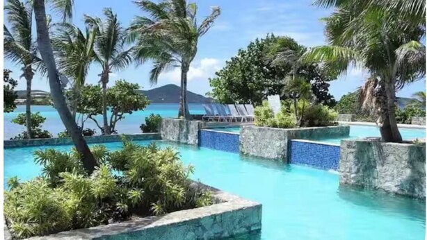 A pool area with clear blue water, surrounded by palm trees and a view of the ocean. - Charming condo walking distance to Sapphire Beach, St Thomas (St Thomas)