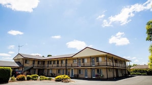 Um motel de dois andares com teto plano, várias varandas e estacionamento.