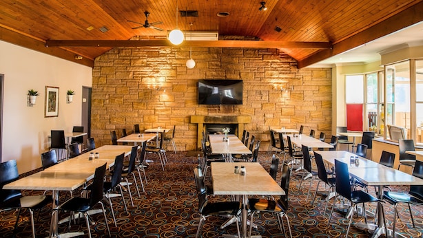 A restaurant with a stone wall, wooden ceiling, and multiple tables and chairs. - Lilac City Motor Inn Standard Queen Room 7 (Goulburn)