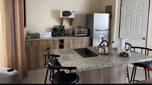 A kitchen with a granite countertop, a microwave, a refrigerator, a toaster, and a kettle.