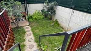 A wooden deck with a small garden area, a red fence, and a view of distant hills.