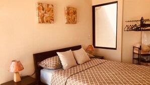 A neatly arranged bedroom with a bed, two wall-mounted artworks, a bedside lamp, and a clothing rack.