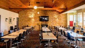 Un restaurante con pared de piedra, techo de madera y varias mesas y sillas.