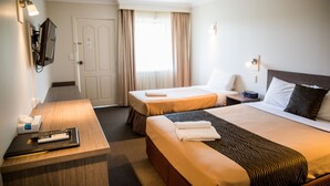 Een hotelkamer met twee bedden, een bureau met afstandsbediening, een aan de muur bevestigde televisie en een raam met gordijnen.