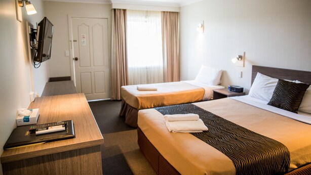 Habitación de hotel con dos camas, un escritorio con control remoto, un televisor en la pared y una ventana con cortinas.