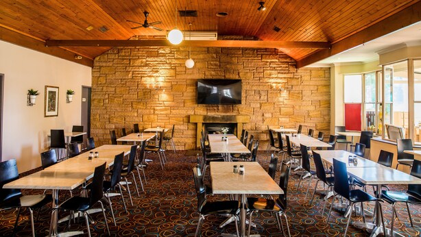 Ein Restaurant mit Steinwand, Holzbalkendecke und mehreren Tischen und Stühlen.