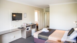 A hotel room with a bed, a desk with a computer, a TV, a microwave, and an air conditioning unit. - Lilac City Motor Inn 2 Room Family 27 (Goulburn)