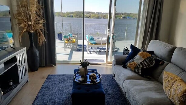 A living room with a sofa, coffee table, and a view of a lake through large sliding doors. - Mississippi Riverfront Retreat - River's Edge - Quad Cities (East Moline)