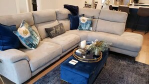 A modern living room with a beige sectional sofa, a blue ottoman, and decorative pillows. - Mississippi Riverfront Retreat - River's Edge - Quad Cities (East Moline)
