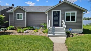 A two-story house with a front porch, a small garden, and a clear sky. - Mississippi Riverfront Retreat - River's Edge - Quad Cities (East Moline)