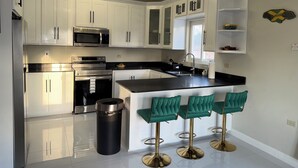 A modern kitchen with white cabinets, stainless steel appliances, a black countertop, and a bar area with green bar stools. - Charming 3-bedroom villa in Ocho Rios with a view of the Caribbean Sea (Ocho Rios)
