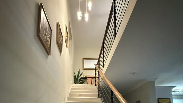 A staircase with a wooden handrail and a black railing, leading to a landing with a framed picture and a potted plant. - Charming 3-bedroom villa in Ocho Rios with a view of the Caribbean Sea (Ocho Rios)
