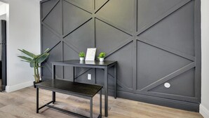 Un interior moderno con un panel de pared geométrico oscuro, un banco de metal negro y pequeñas plantas en macetas.