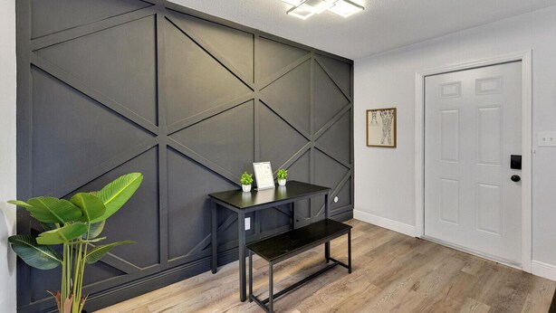 Un pasillo moderno con una pared de acento oscura, una pequeña mesa con una planta y un cuadro en la pared.