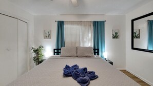 Una camera da letto con un letto, un ventilatore a soffitto, un comodino, una lampada e una finestra con tende.
