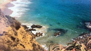 A coastal view with clear blue waters, sandy beach, and rocky outcrops.