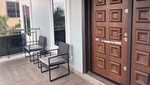 A balcony with a glass railing, two wicker chairs, and a wooden door with decorative panels. - Spacious 2BR private apartment setting for families near Accra. (Oyibi)