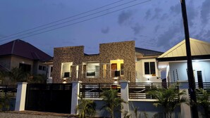 A modern house with a stone facade, a gated entrance, and a well-lit interior. - Spacious 2BR private apartment setting for families near Accra. (Oyibi)