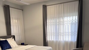 A bedroom with a bed, a chair, a ceiling fan, and a window with curtains. - Spacious 2BR private apartment setting for families near Accra. (Oyibi)